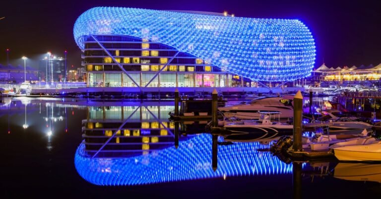 Modern hotel with vibrant blue lights reflecting in calm waters at night.